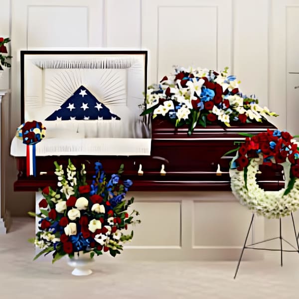 Red, white, and blue funeral floral tributes around a casket draped with a U.S. flag