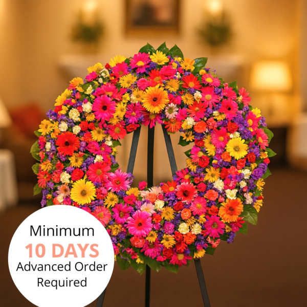Bright circular standing wreath of mixed pink, orange, yellow, and purple flowers on a black easel indoors