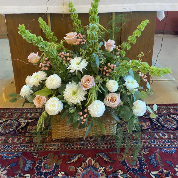 Large floral arrangement with pale roses, white blooms, and green spikes in a woven basket