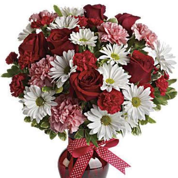 Red roses, white daisies, and pink carnations in a red vase with a ribbon