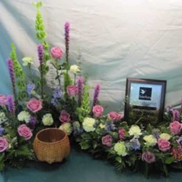 Floral arrangement with pink roses and tall purple spikes around a framed plaque
