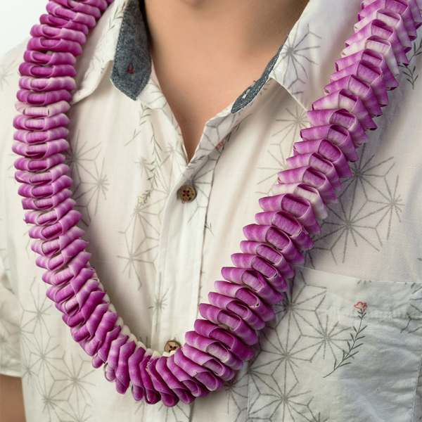 Purple orchid petal lei worn around a person’s neck over a patterned shirt