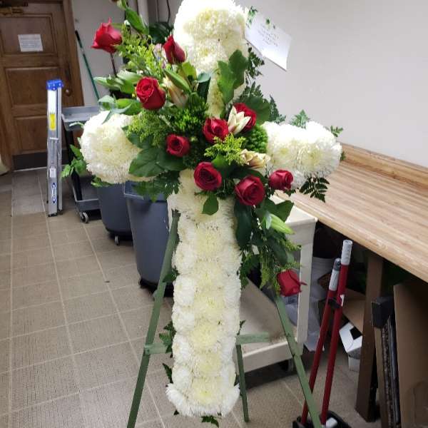 Standing floral cross with white blooms and red roses on an easel