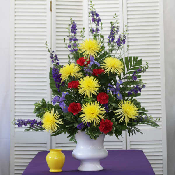 Tall floral arrangement in a white vase with yellow, red, and purple flowers