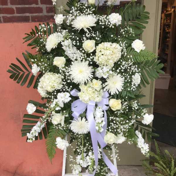 White floral standing spray with a lavender ribbon on an easel