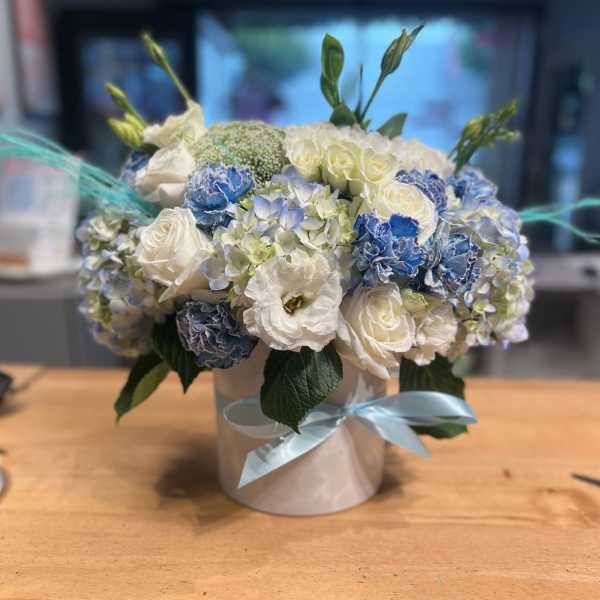 Blue and white flower arrangement in a round box with ribbon