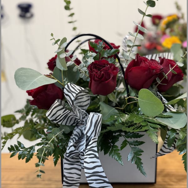 Red roses in a white box with zebra-print ribbon and greenery