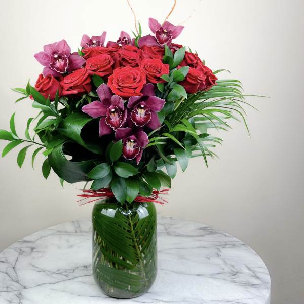 Bouquet of red roses and purple orchids in a glass vase