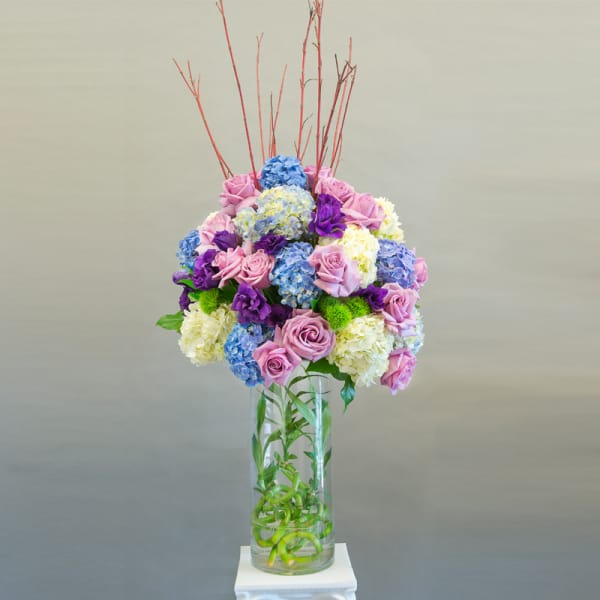 Tall bouquet of pink roses, blue hydrangeas, and purple flowers in a glass vase