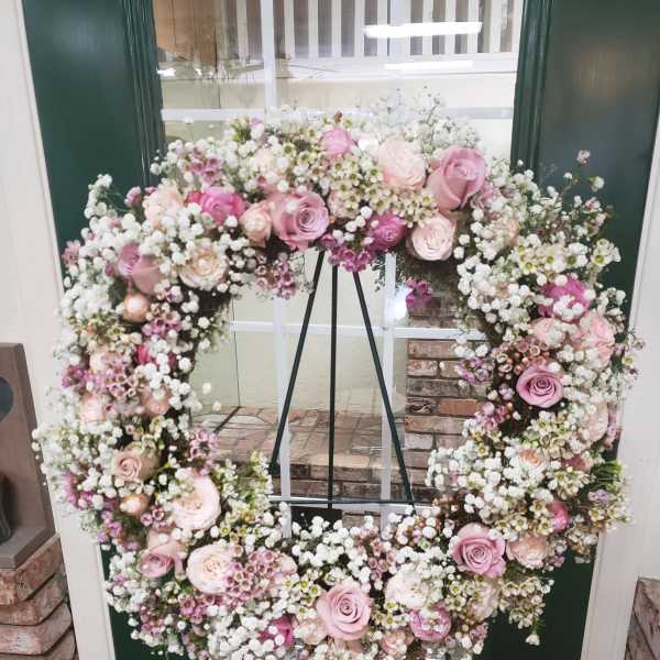 Heart-shaped floral wreath with pink roses and white baby's breath on an easel