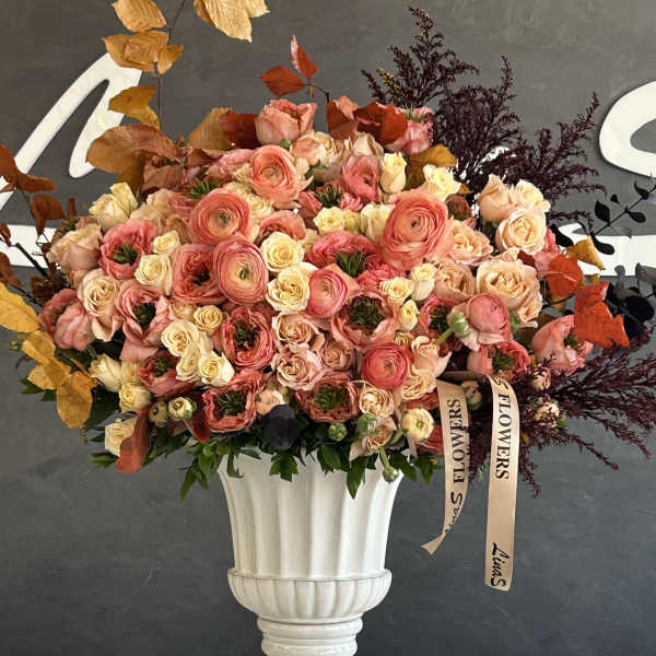 Large pink and peach rose arrangement in a white pedestal vase