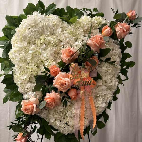 Heart-shaped white floral wreath with peach roses on a stand