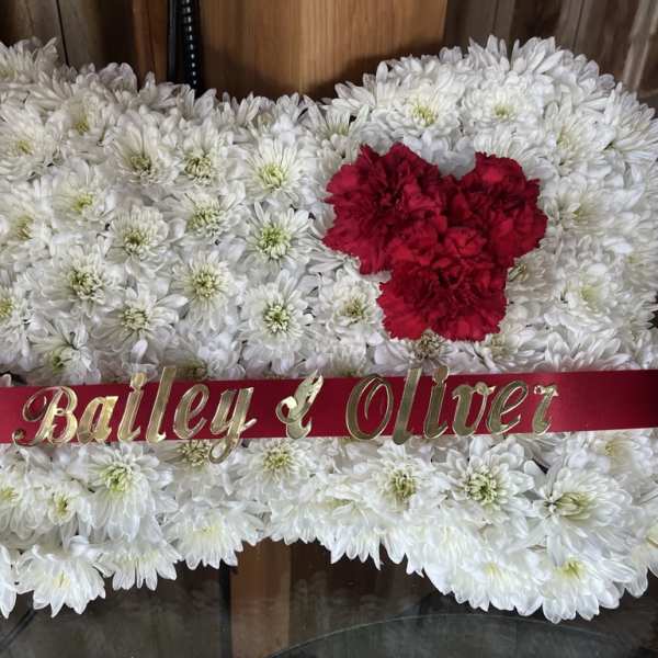 White chrysanthemum arrangement with red carnations and a name ribbon