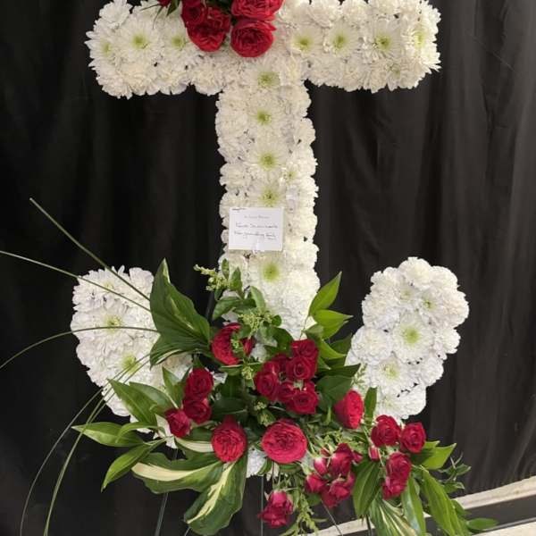 White floral cross with red roses and greenery on a black backdrop