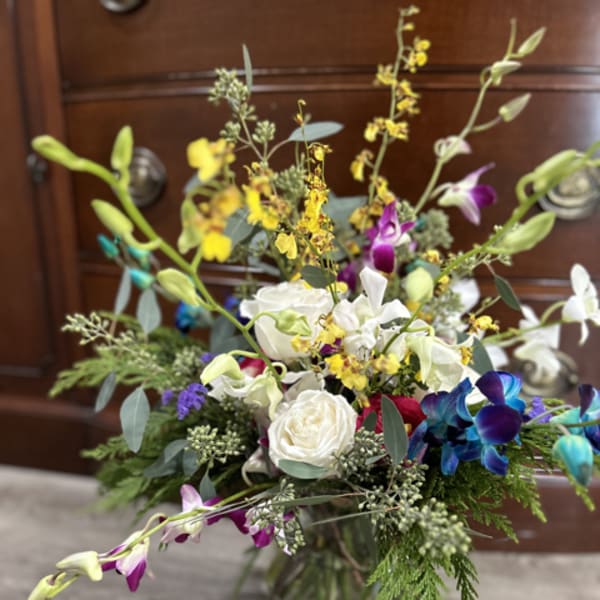 Mixed bouquet with white roses, orchids, and yellow accents in a glass vase