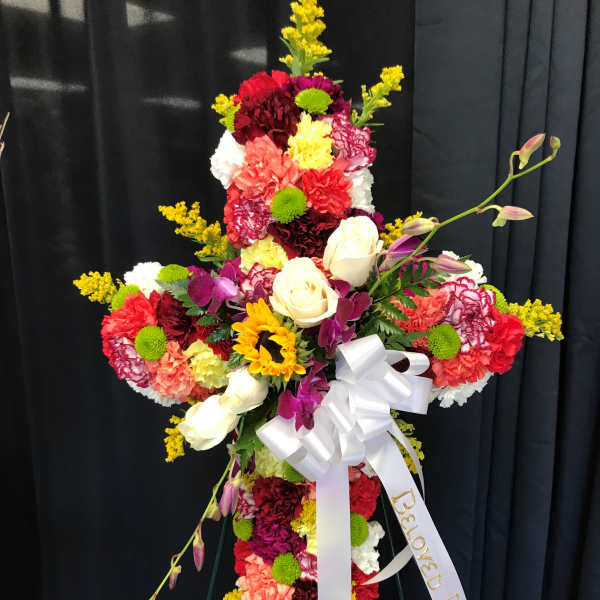 Standing cross of mixed bright flowers with roses and sunflower, white bow, and 'Beloved Brother' ribbon.