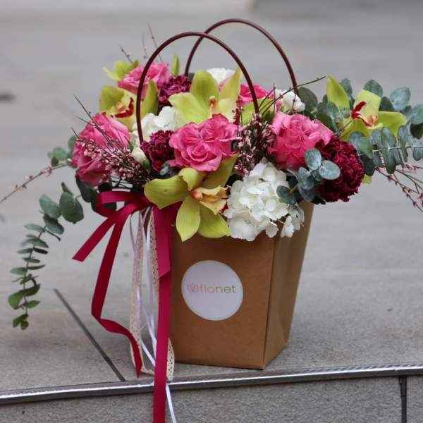 Pink and white flower arrangement in a brown gift bag with ribbon handles