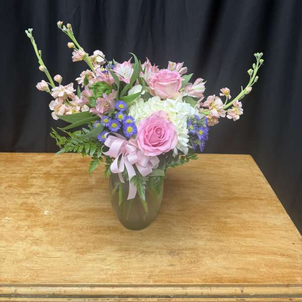 Pink roses and mixed flowers arranged in a glass vase with a ribbon
