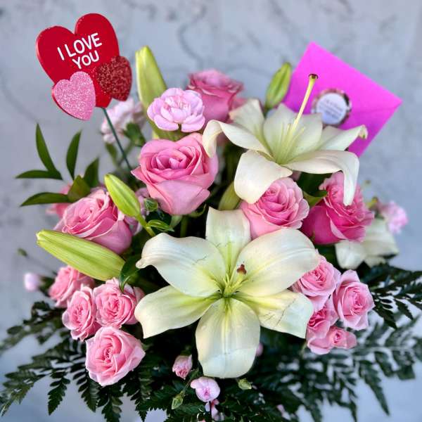 Pink roses and white lilies in a bouquet with an "I LOVE YOU" pick