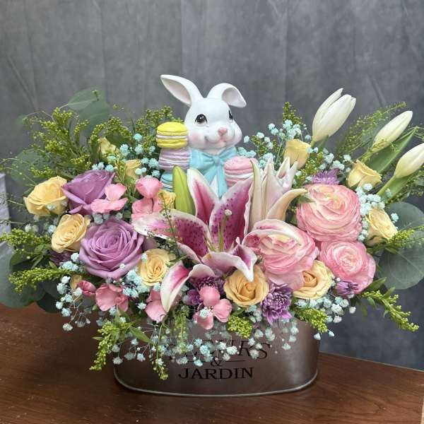 Pastel flower arrangement with lilies, roses, and a ceramic bunny in a metal container.