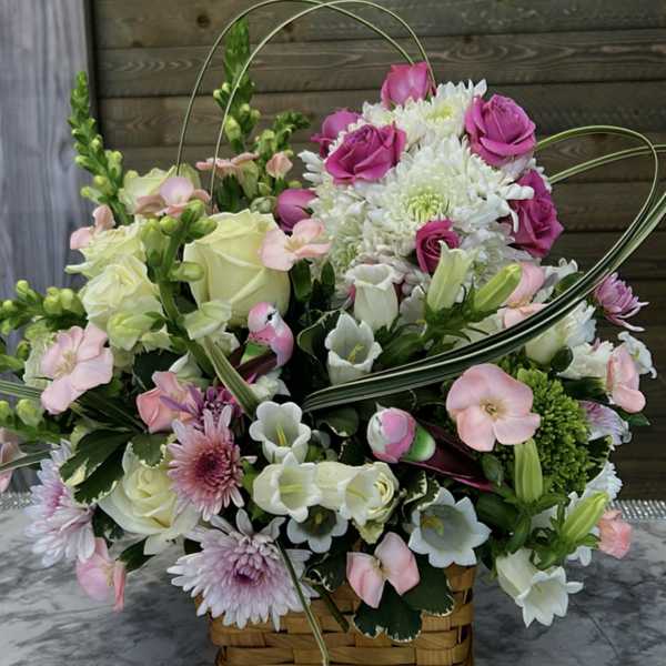 Basket arrangement of pink and white flowers with curved decorative loops