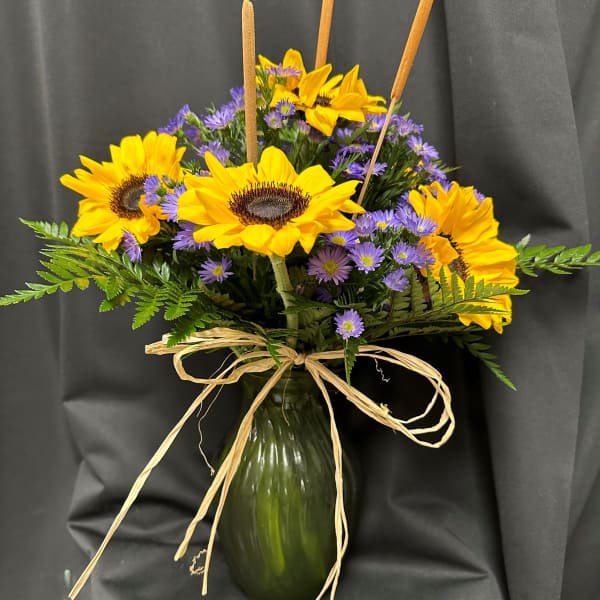 Sunflowers and purple daisies in a green glass vase with cattails