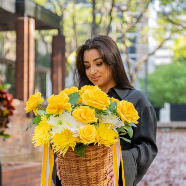 Woman holding a basket of yellow roses and white flowers with ribbon streamers