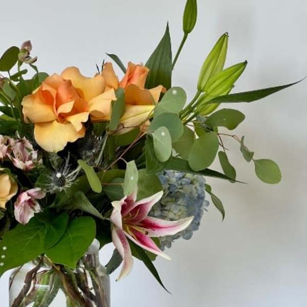 Bouquet of peach roses, lilies, and blue hydrangea in a glass vase