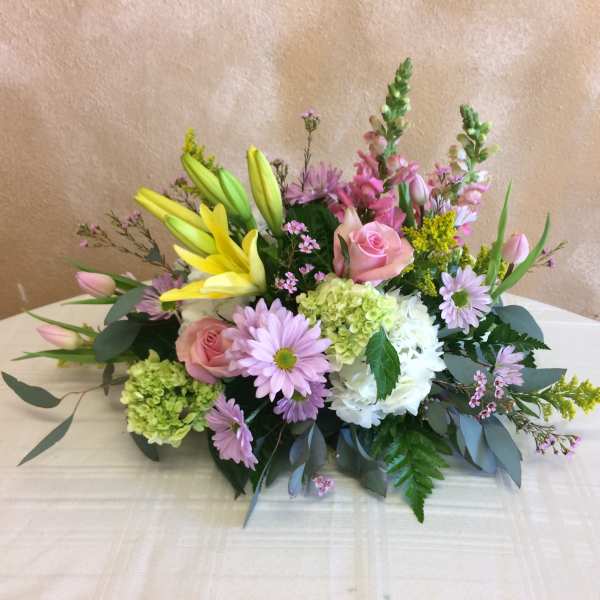 Low pastel centerpiece with yellow lilies, pink roses, tulips, and mixed blossoms.