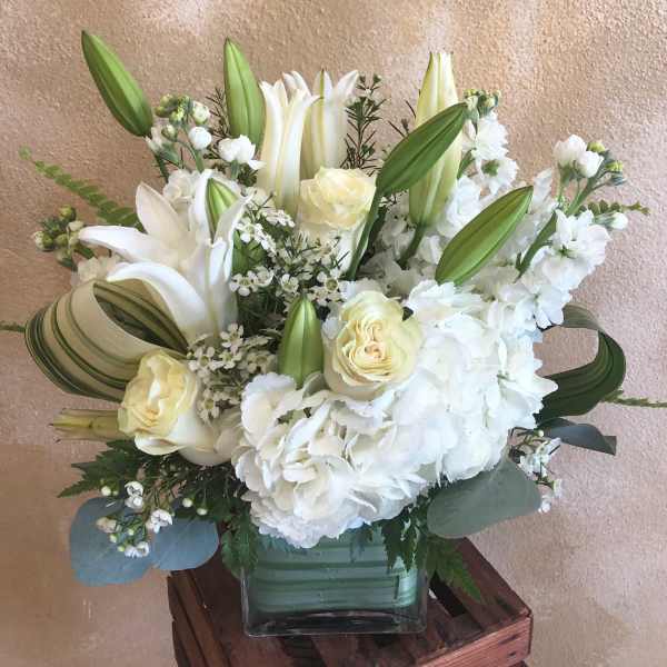 White lilies and roses arranged in a square glass vase