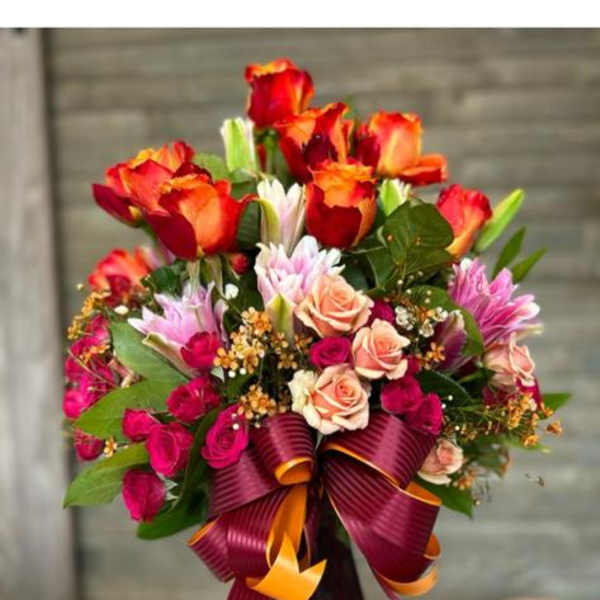 Bouquet of red and peach roses in a burgundy vase with a ribbon bow