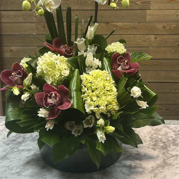 White orchids and burgundy orchids in a low black bowl arrangement