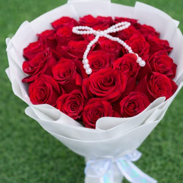 Bouquet of red roses wrapped in white paper with a pearl ribbon