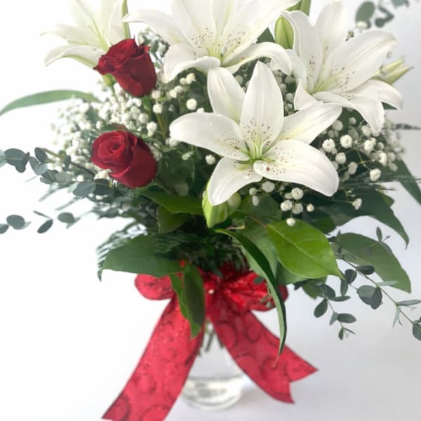 Bouquet of white lilies and red roses in a glass vase with a red ribbon