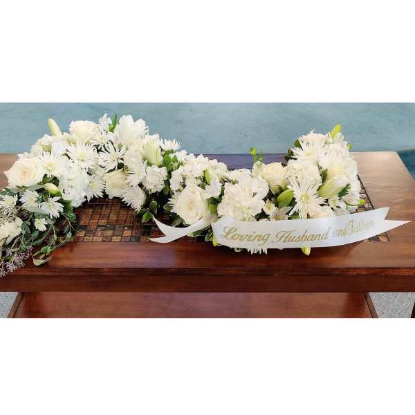 White funeral floral arrangement with a ribbon on a wooden table