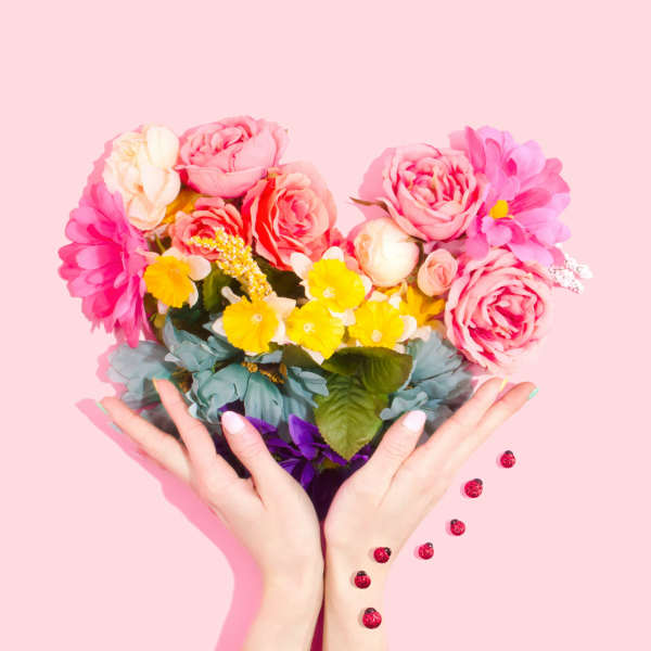 Hands holding a colorful bouquet of pink, yellow, and white flowers