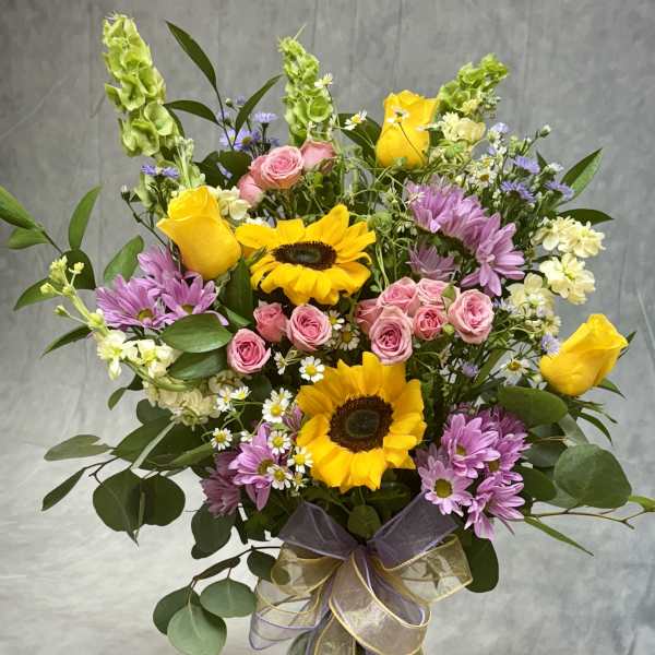 Bouquet of yellow sunflowers, pink roses, and purple daisies in a glass vase