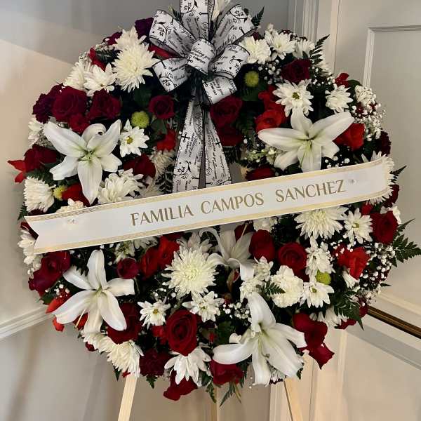 Standing round wreath of red roses, white lilies, and white mums with script ribbon on an easel