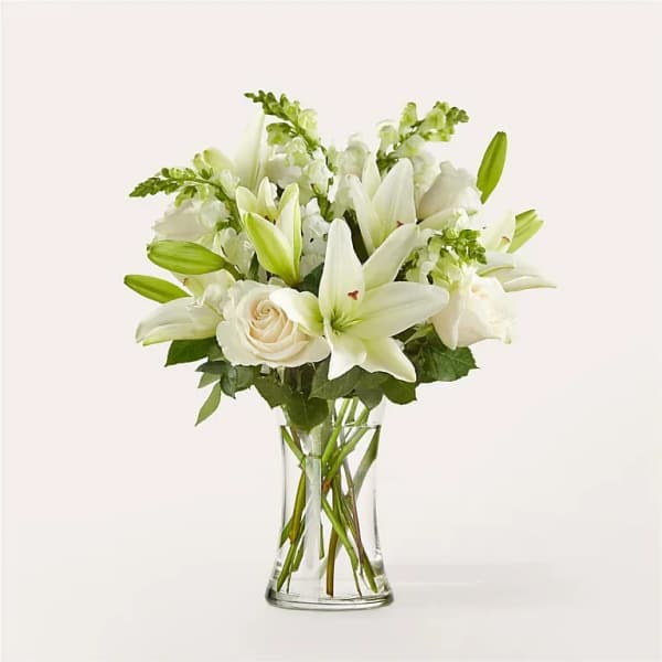 White lilies and roses arranged in a clear glass vase with visible stems.
