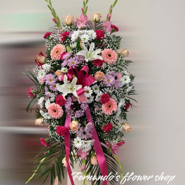 Tall standing spray of pink, white, and peach flowers with a pink ribbon on an easel