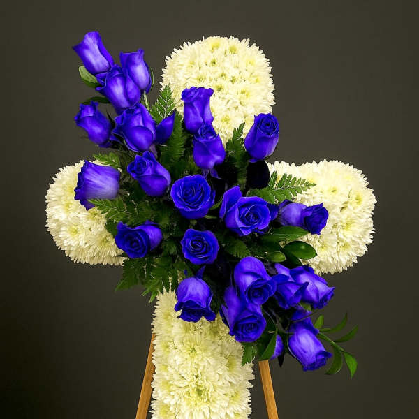 Standing white chrysanthemum cross with cluster of vivid blue roses on a wooden easel