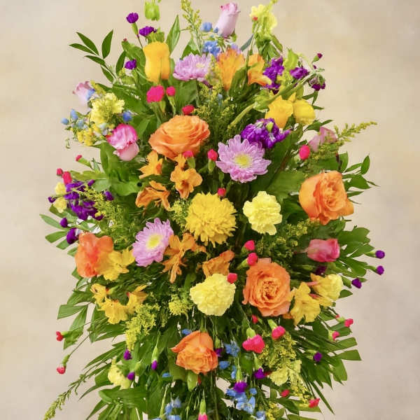 Tall multicolor standing spray with orange roses and yellow blooms on a metal easel