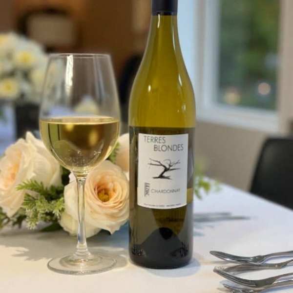 Wine bottle and glass beside a small cream rose arrangement