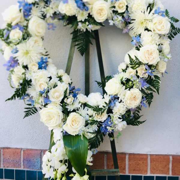 Heart-shaped floral wreath with white roses and blue flowers on an easel