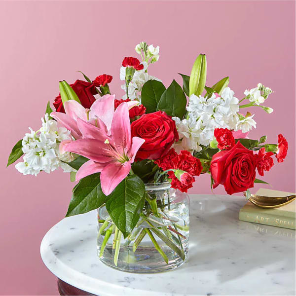 Pink lilies, red roses, and white flowers in a clear glass vase