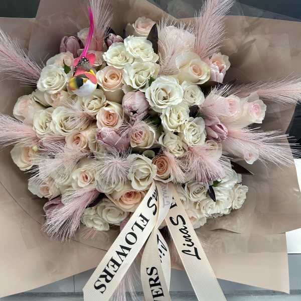 Bouquet of cream and blush roses with pink feathers and a ribbon bow