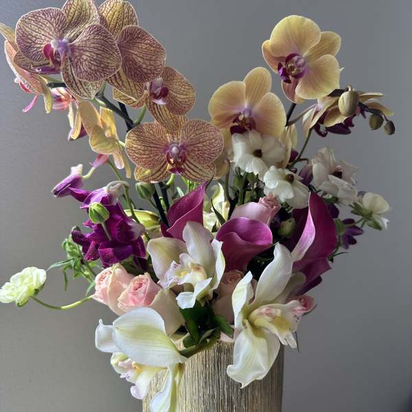 Mixed orchid arrangement in a gold textured vase