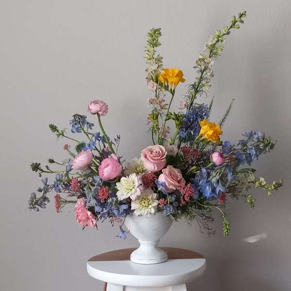Pastel mixed flower arrangement in a white pedestal vase