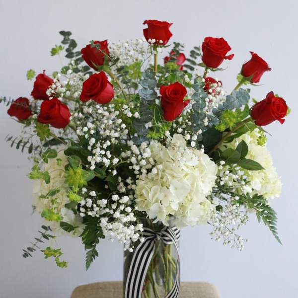 Red roses and white hydrangeas in a glass vase with a striped ribbon