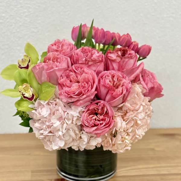 Pink roses and hydrangeas in a black vase with green orchids